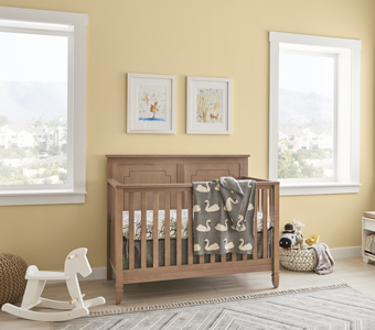 A decorated baby nursery with light yellow walls, a wooden crib, and a white rocking horse.