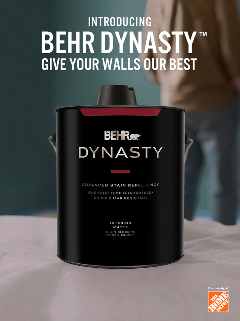 Couple getting ready to paint with a can of BEHR DYNASTY Flat interior paint and the words Introducing BEHR DYNASTY Give Your Walls Our Best in foreground.