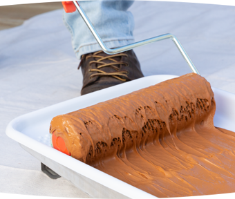 Person rolling a paint roller into a tray of stain