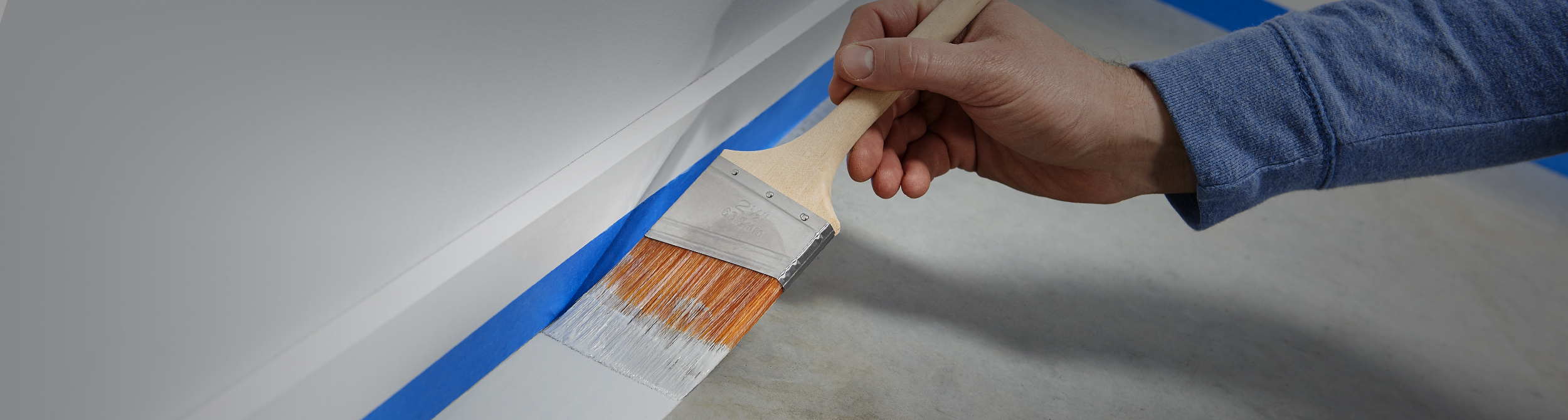 Person painting a concrete floor along baseboard.