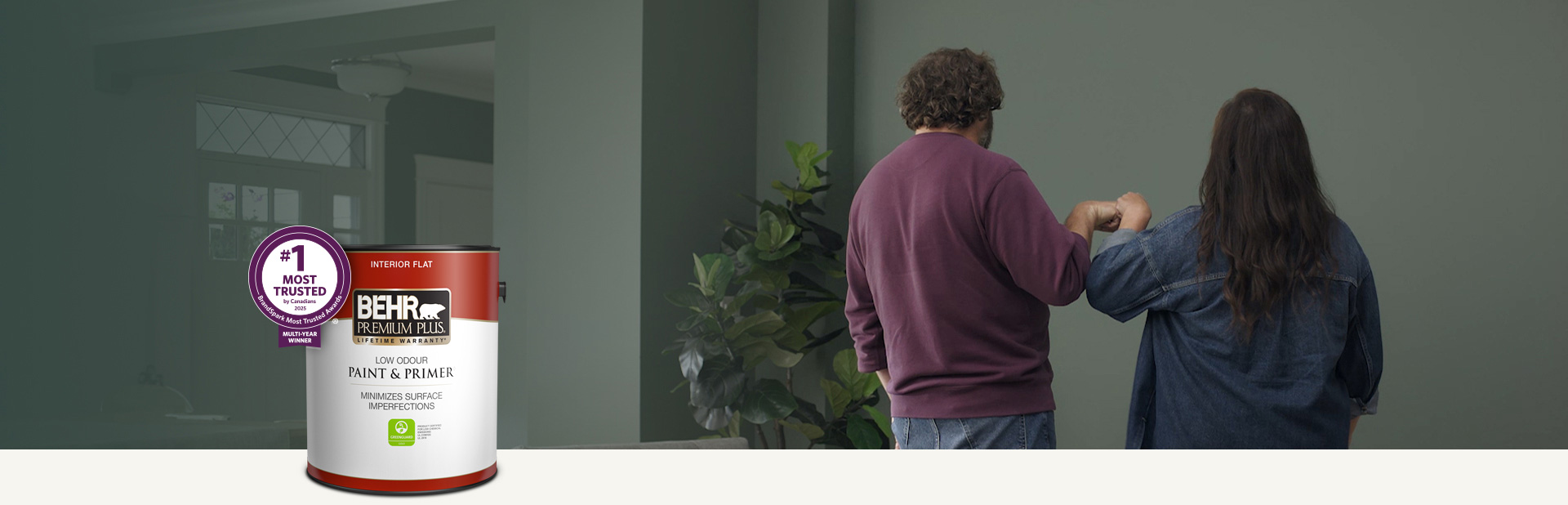 Choir standing in a painted living room and holding a can of Behr Premium Plus Interior Flat Paint