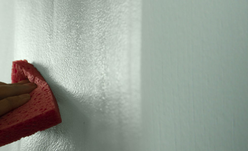 Person's hand scrubbing a stain off the wall with a sponge