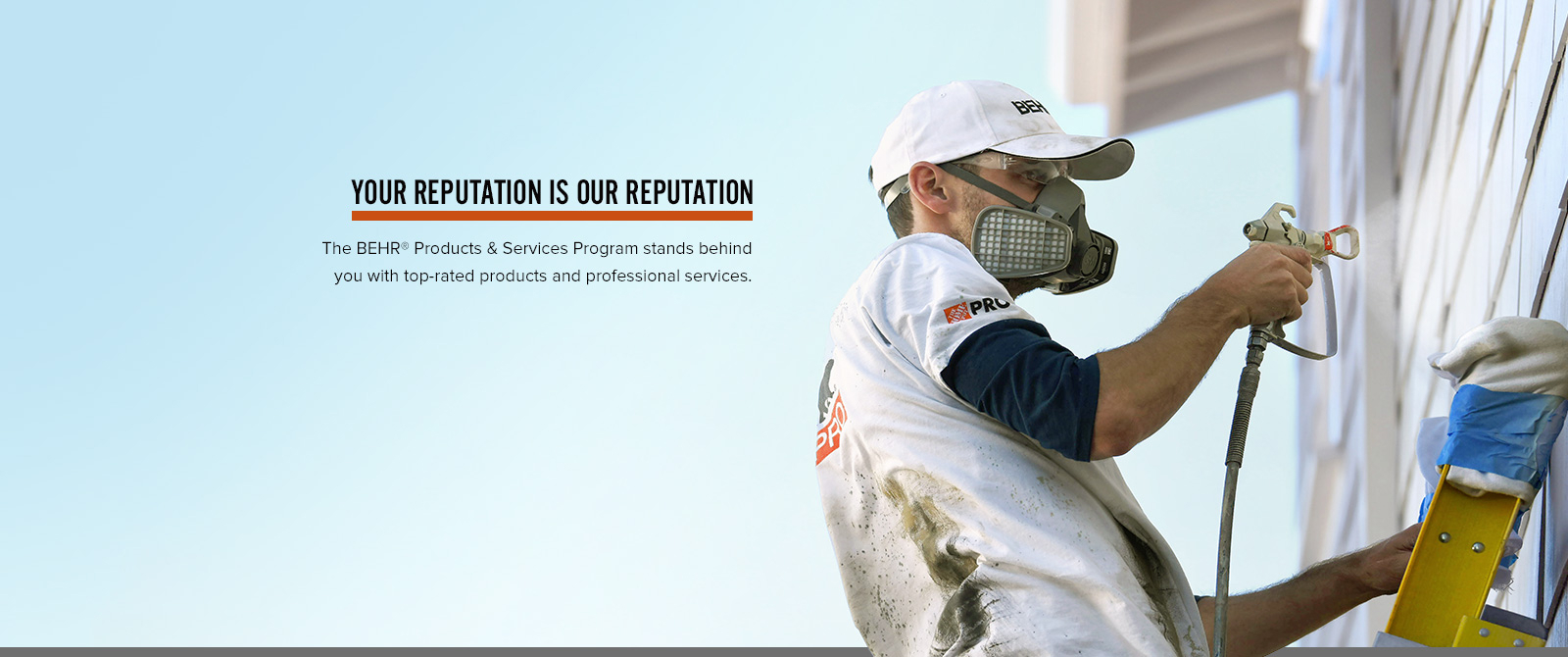 Image of a Pro Contractor wearing a hat and shirt with Behr logo spray painting an exterior wall of a house on a ladder.