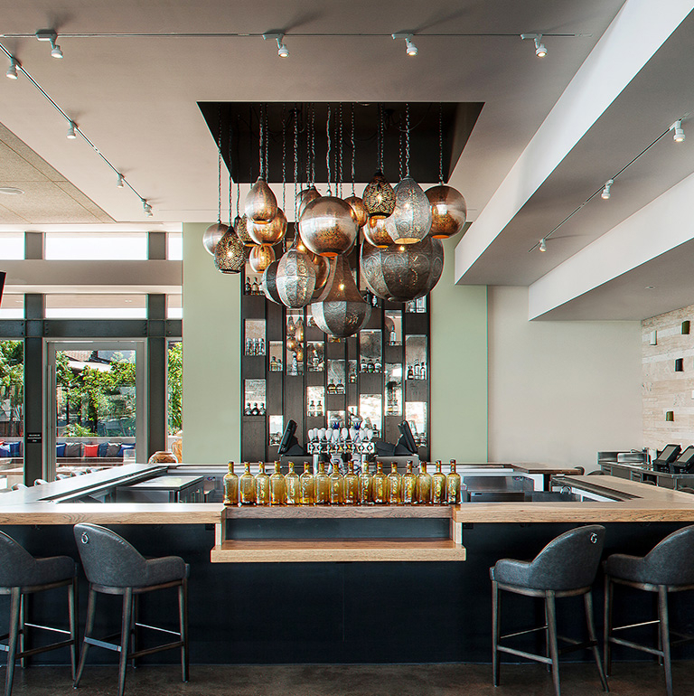 Image of an empty modern bar. In the middle of a bar there are Moroccan lamps hanging from the ceiling and you can see the outside from the inside of the bar