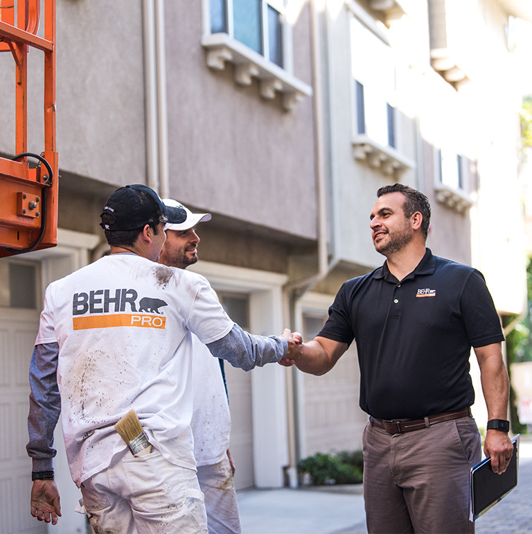 A mobile view of a BEHR PRO Rep shaking hands with on of the 2 Pro Painters. In the background is a multi family condo units.