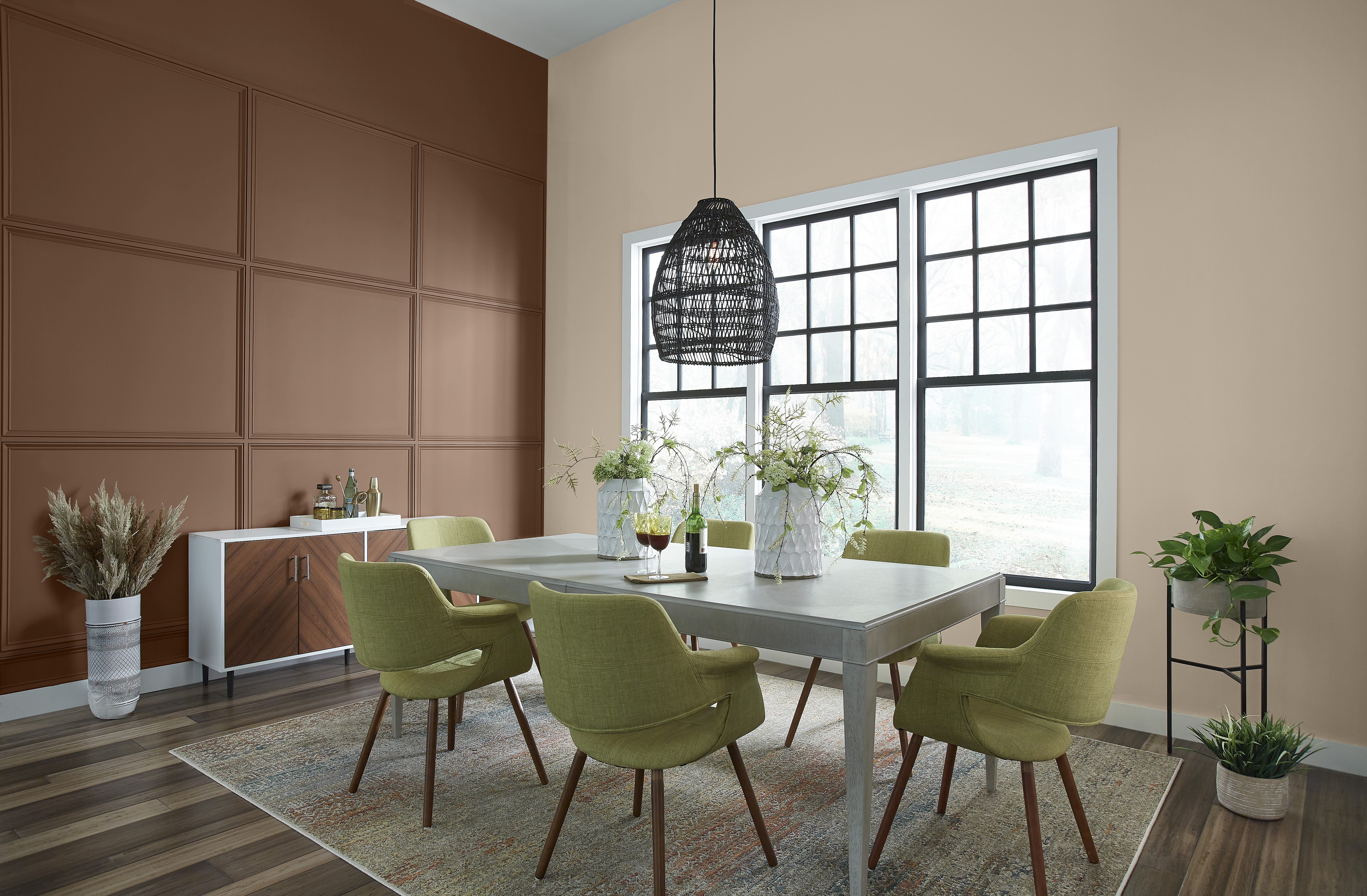 An eclectic dining room with modern table and green upholstered chairs.  An accent wall is paint with a brown color called Wild Mustang. 