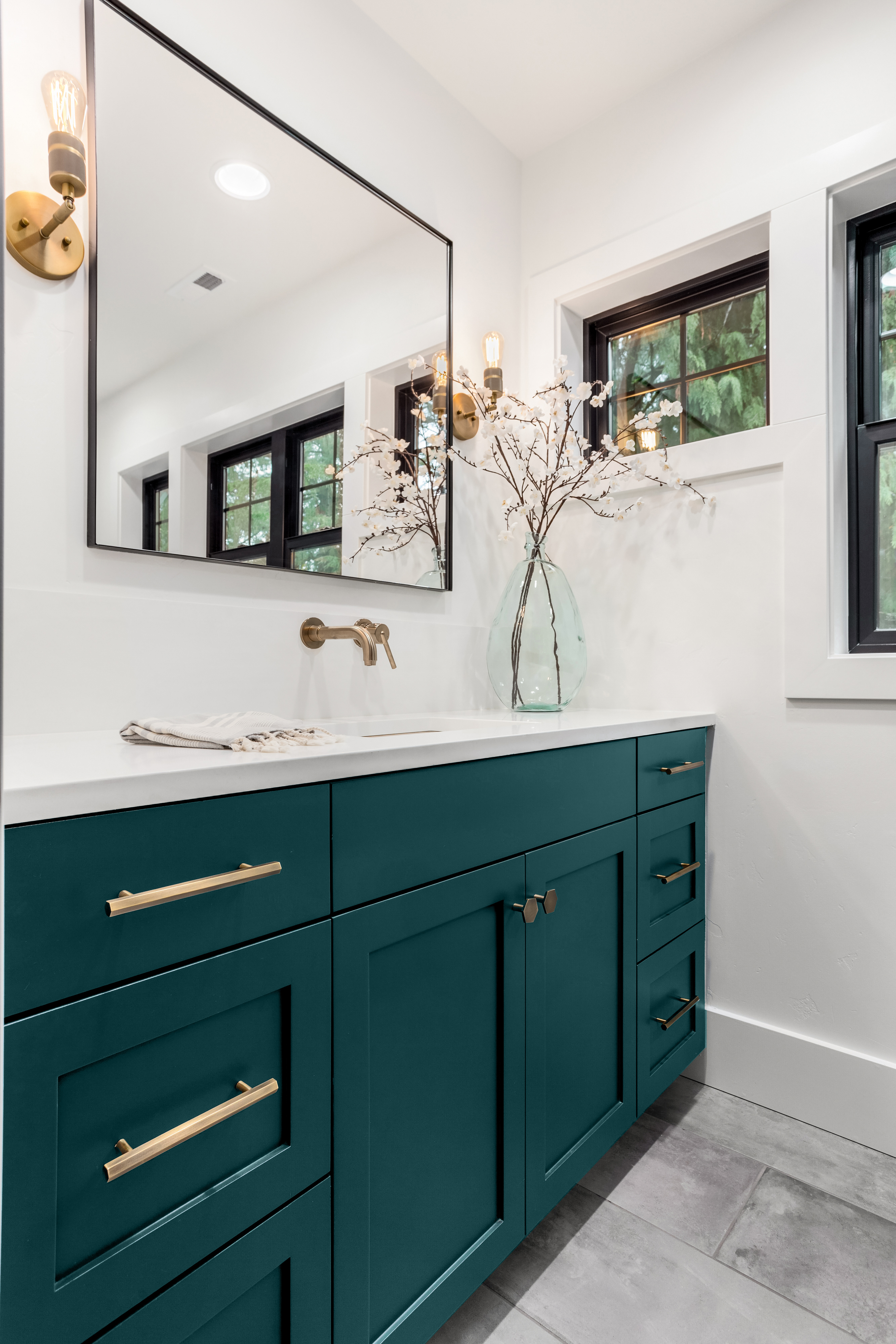 A bathroom with beautiful cabinets and finishes. The cabinet was painted in glossy deep teal color called Ocean Abyss. The hardware throughout  the cabinets is metallic gold or brassy colors.  