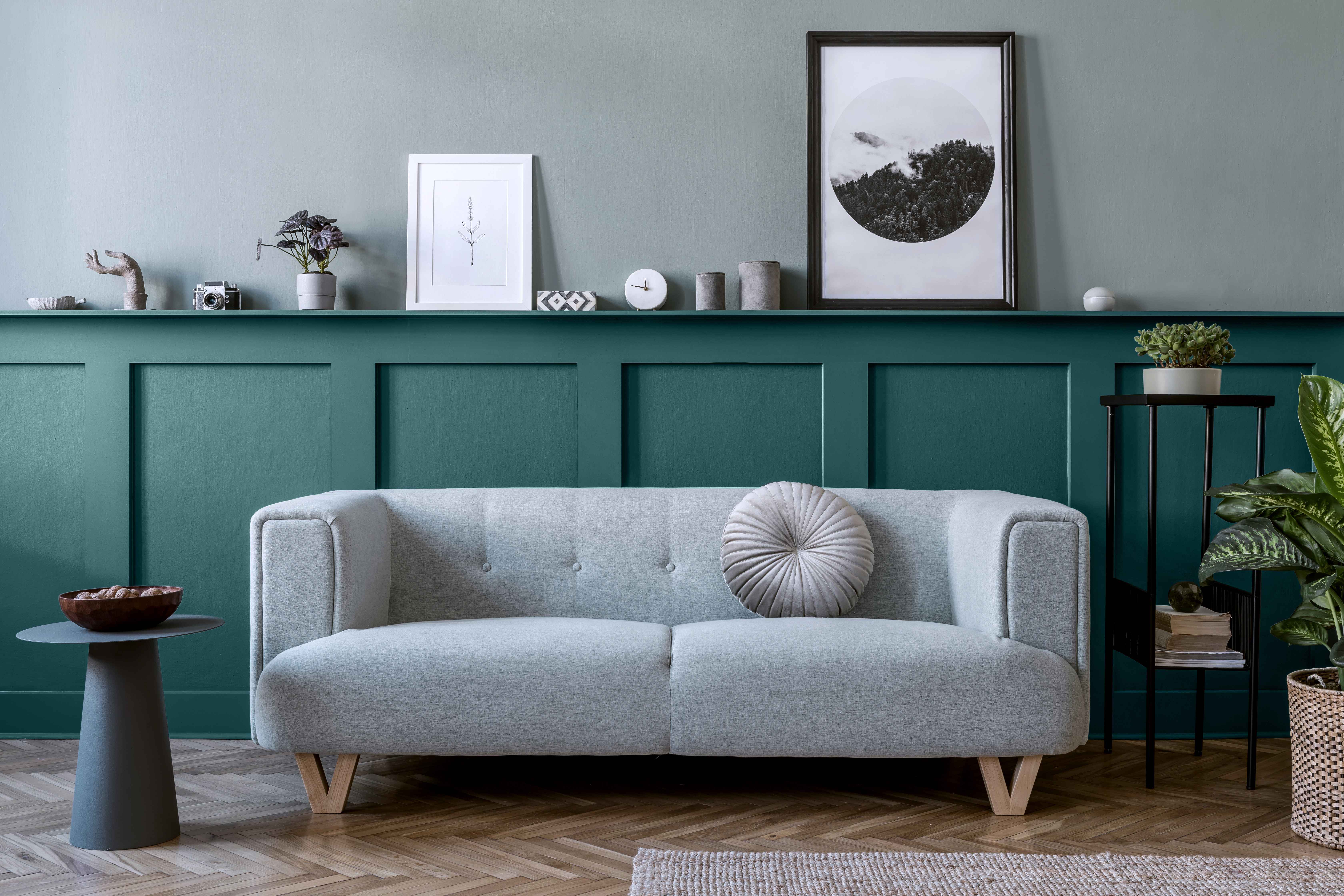 A living room featuring a lower accent wall.  The top of the wall is painted in an almost neutral blue-green color called Water.  The accent lower wall is called Ocean Abyss.  The room is decorated with neutral casual decorative elements raging from a light gray upholstered sofa, a black tall side table, and concrete gray color small decorative elements. 