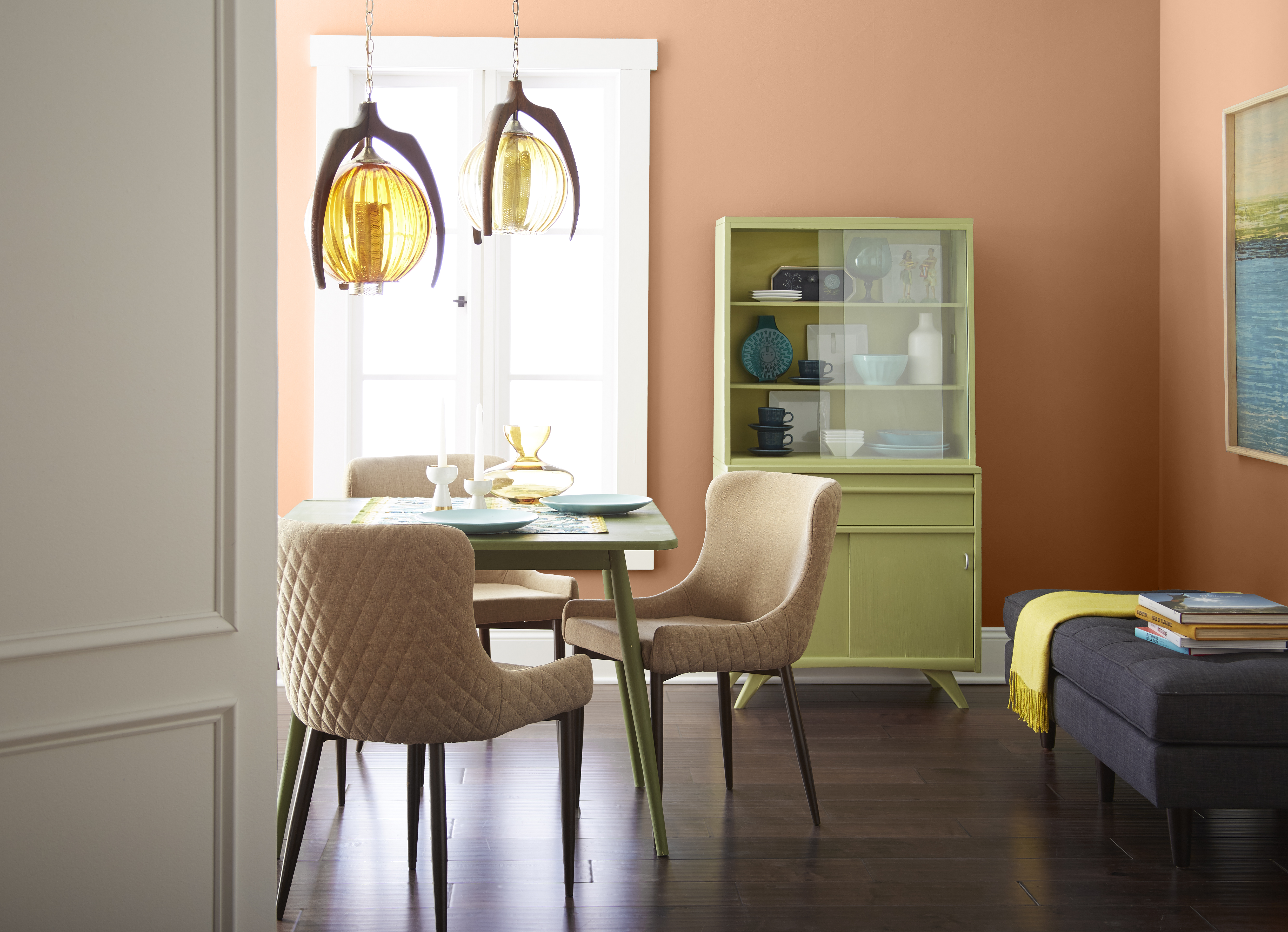 A mid-century dining room area with retro furniture pieces painted in bright pastel yellow-green color.  The terra cotta color on the wall coordinates nicely with the furniture keeping it from looking for bright but rather warm and welcoming. 
