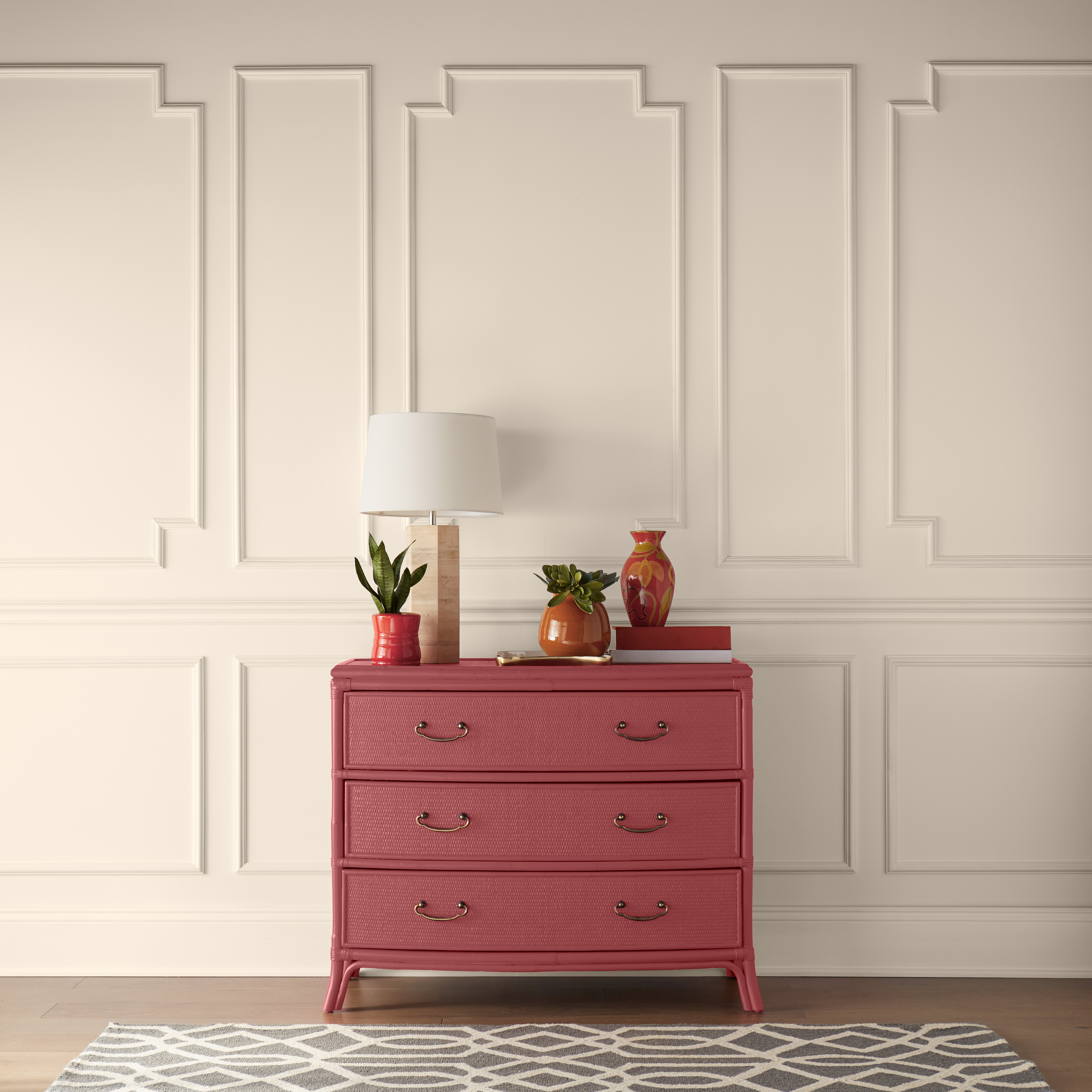 A hallway with a red dresser, the paint color is called Lingonberry Punch. 
The dresser is decorated with red and orange vases and planters. 