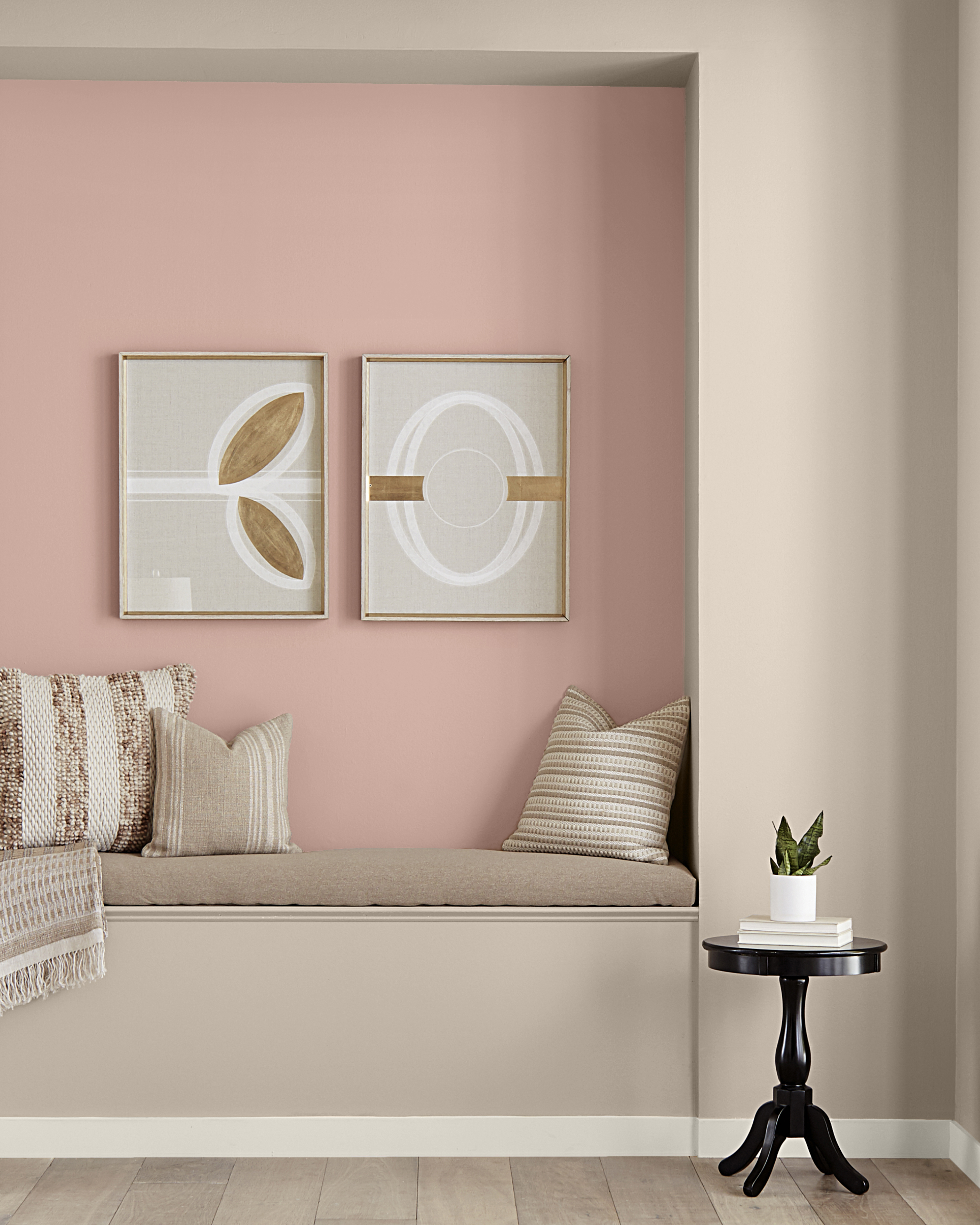 Hallway reading nook with accent wall in pink hue. Accent wall has two picture frames with decorative print. Seating area with neutral tones. 