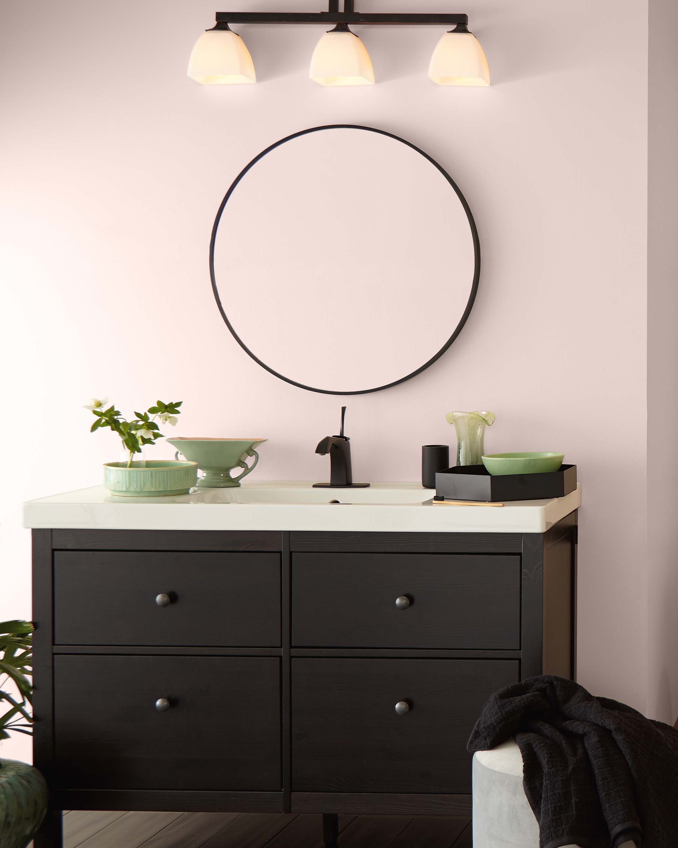 Bathroom image that showcases sink vanity. Decor in sage green accents. Circular mirror and walls painted in Stolen Kiss a delicate light rose tone.