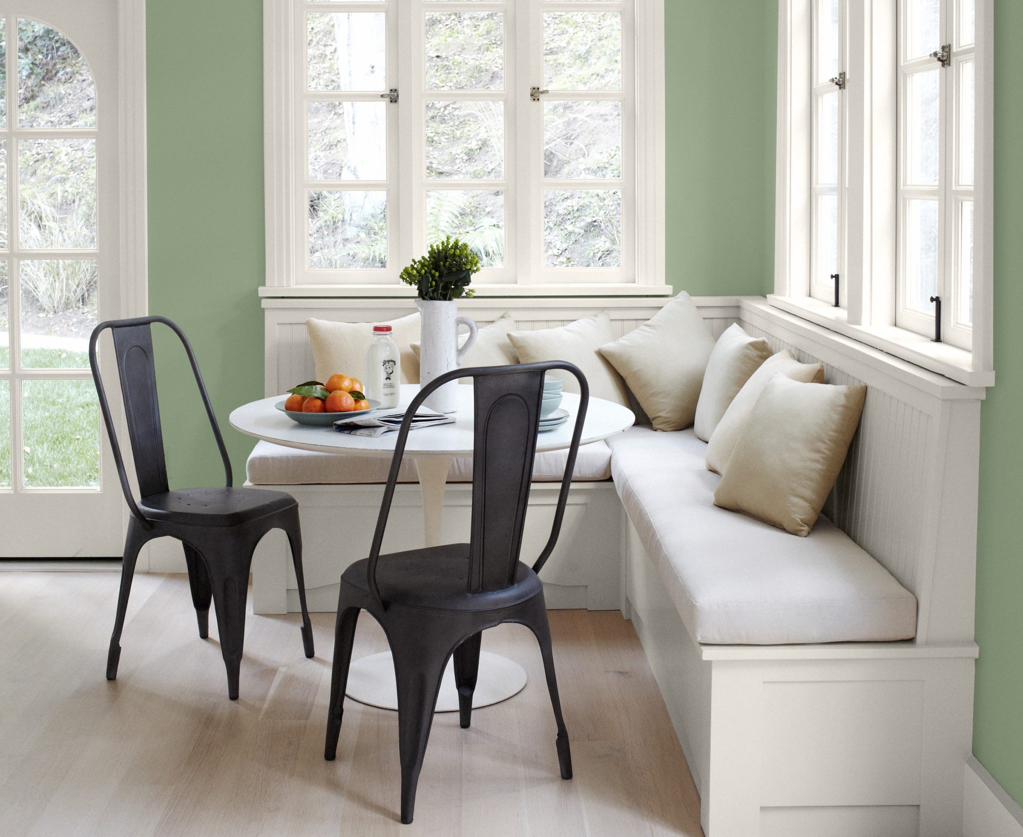 A farmhouse style breakfast nook with comfy bench and metal chair.  The walls are painted in a green color called Laurel Tree. 