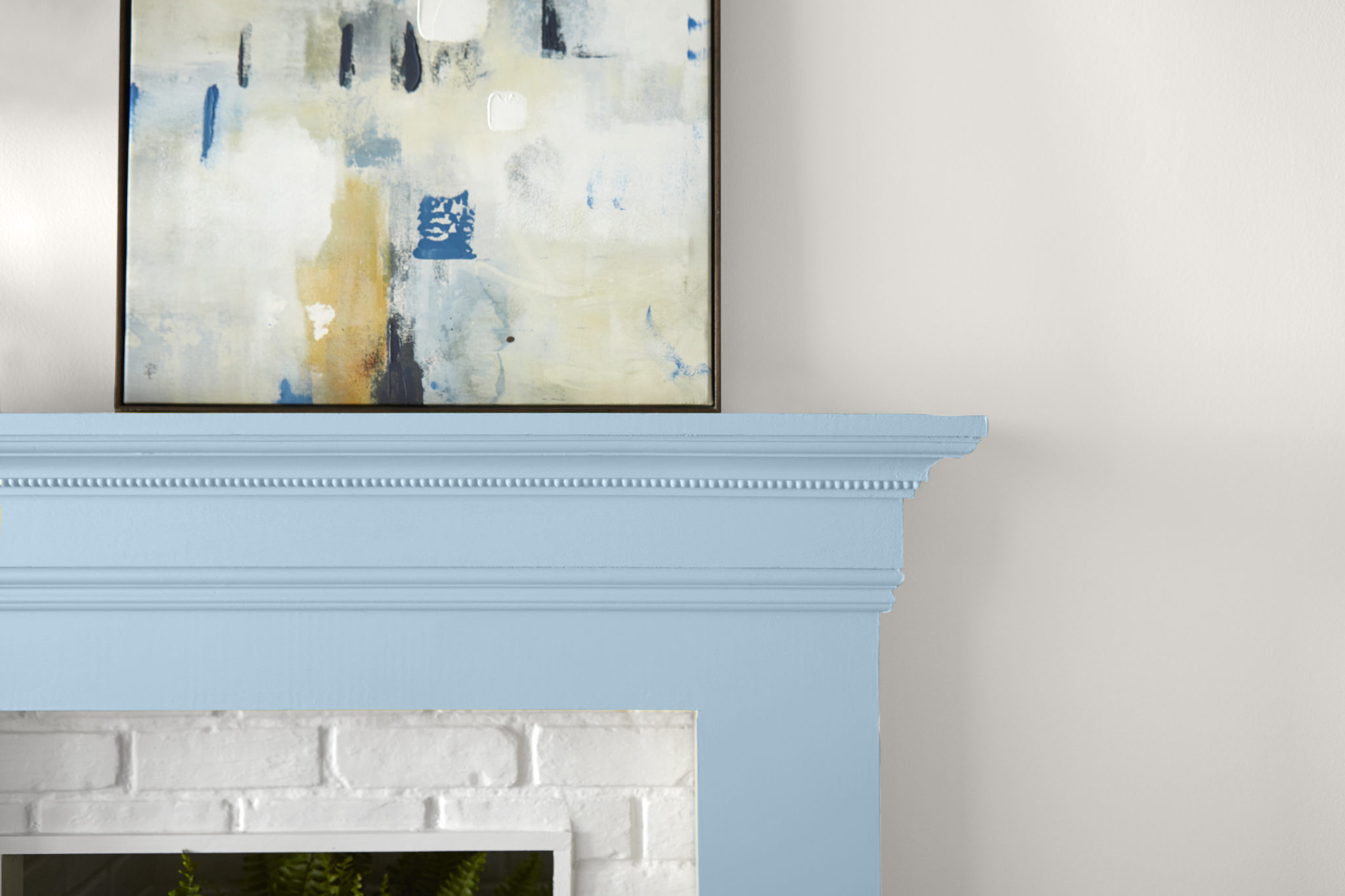 A white wall with a fireplace mantle painted in a light blue color called, After Rain. Abstract wall art completes the look.