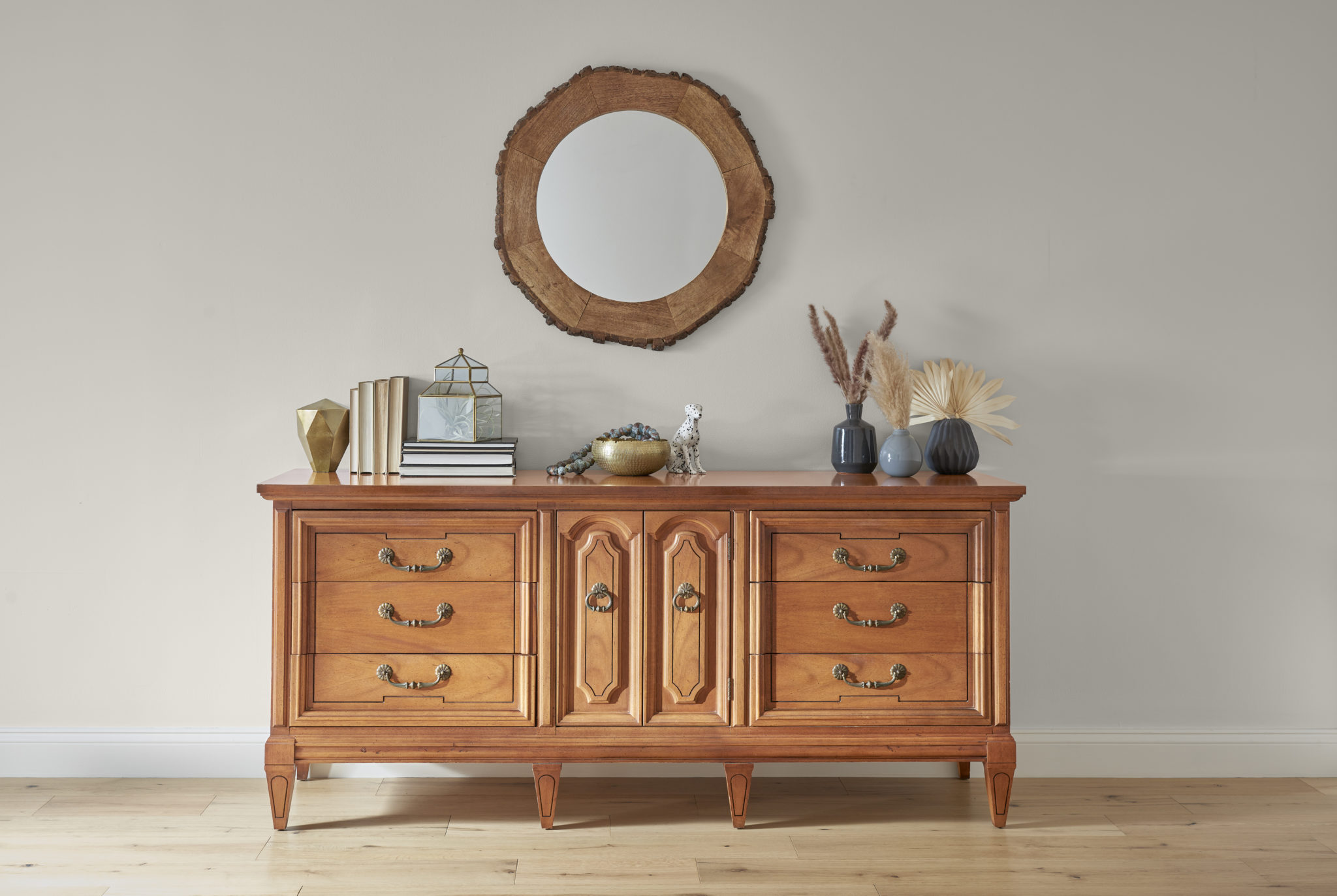 Photo of dresser decorated with books, and other decor pieces. Above the dresser is a wooden mirror. 