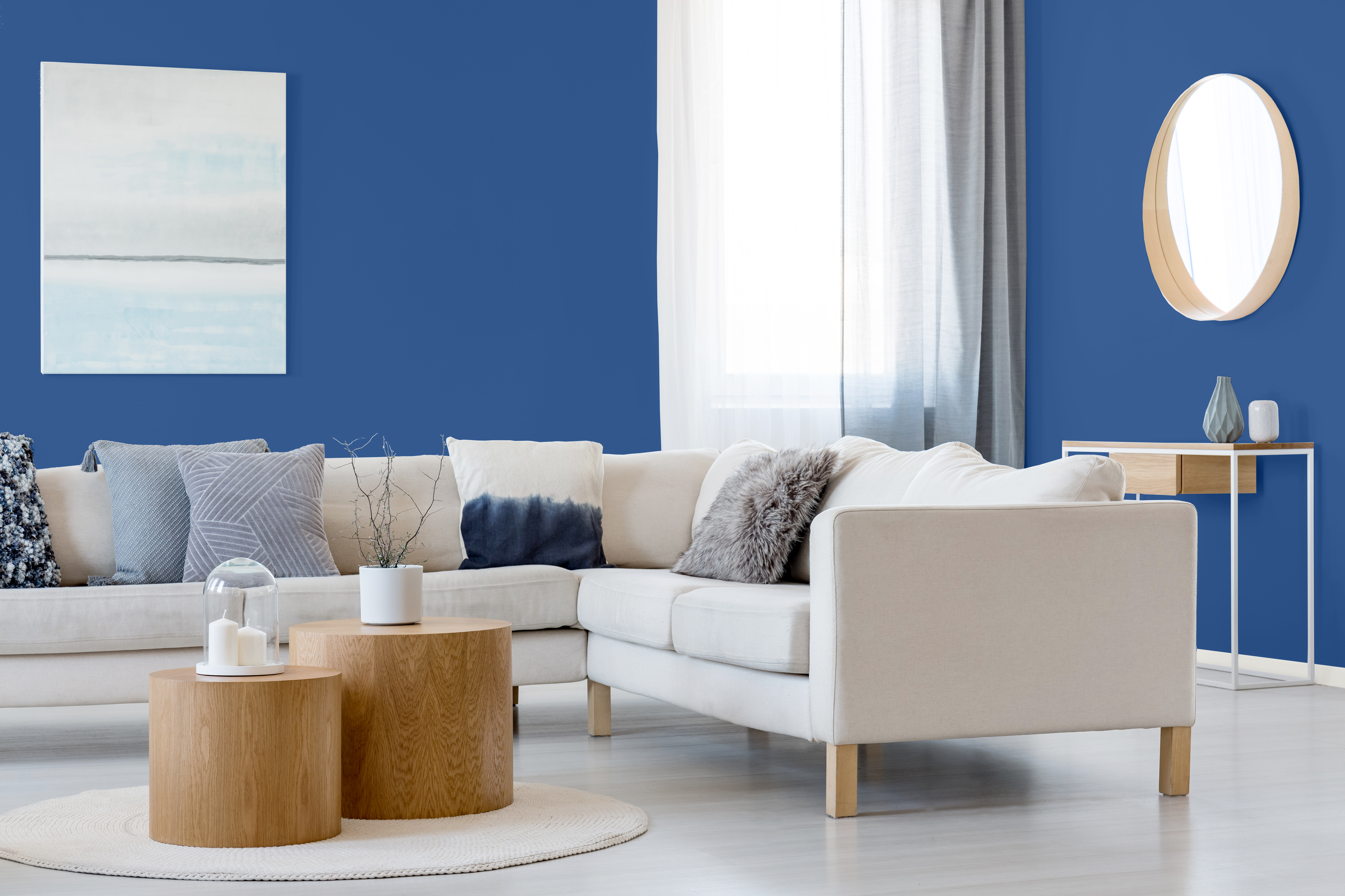 Blue and white abstract painting and mirror in wooden frame in elegant living room interior with corner sofa and coffee table.