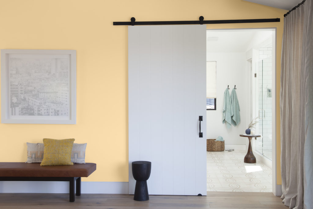 A hallway - bathroom entrance.  The hallway is painted with a warm and inviting yellow called Corn Stalk. The bathroom entrance features are sliding door. 