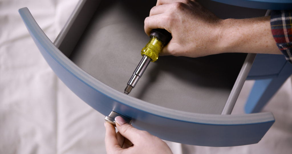 A person taking off the knobs of a drawer from the nightstand.