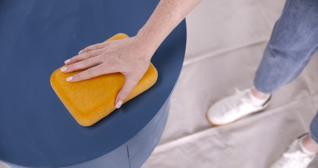 A person using a sponge to clean the top of a nightstand.