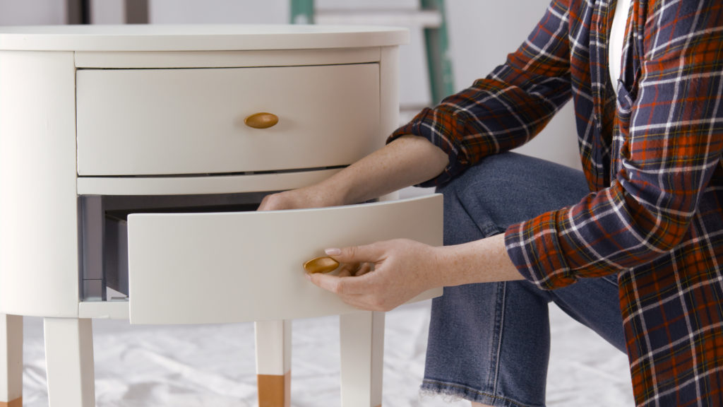 a person placing gold knobs onto a white nightstand.