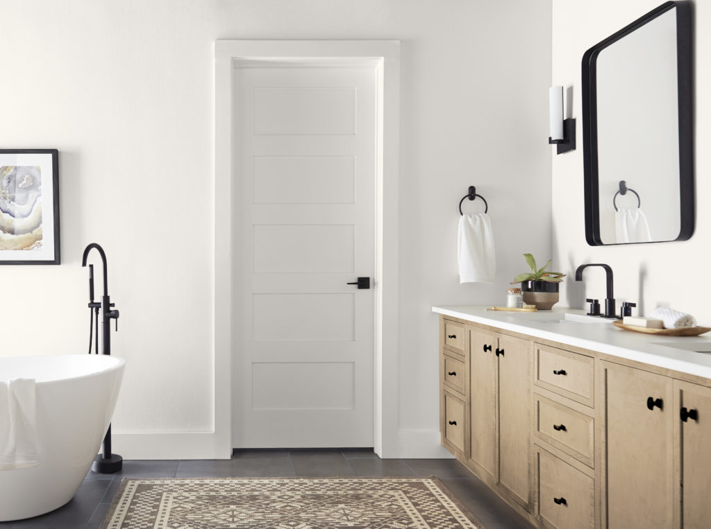 A bathroom with white walls, doors, and moulding looks stunning when paired with black industrial fixtures and rustic wood accents. 