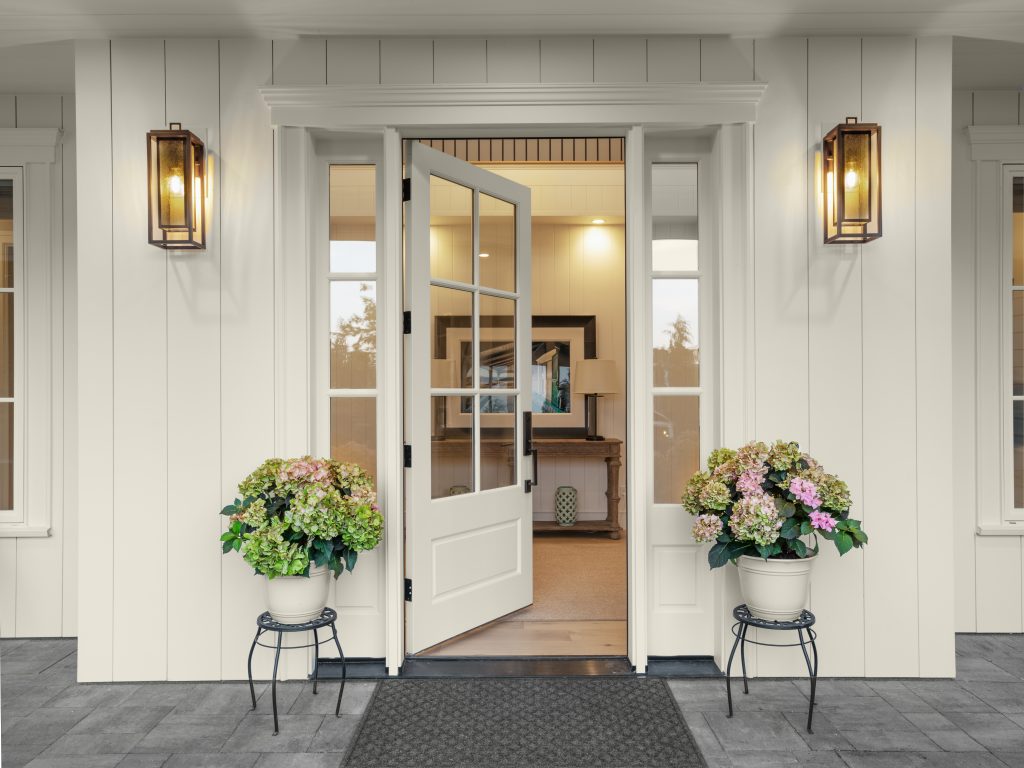 An all-over white home front entry with an open door, the few but carefully selected decorative plants and simple lighting fixtures creates a sense of peace and grace. A great example of “less is more”.