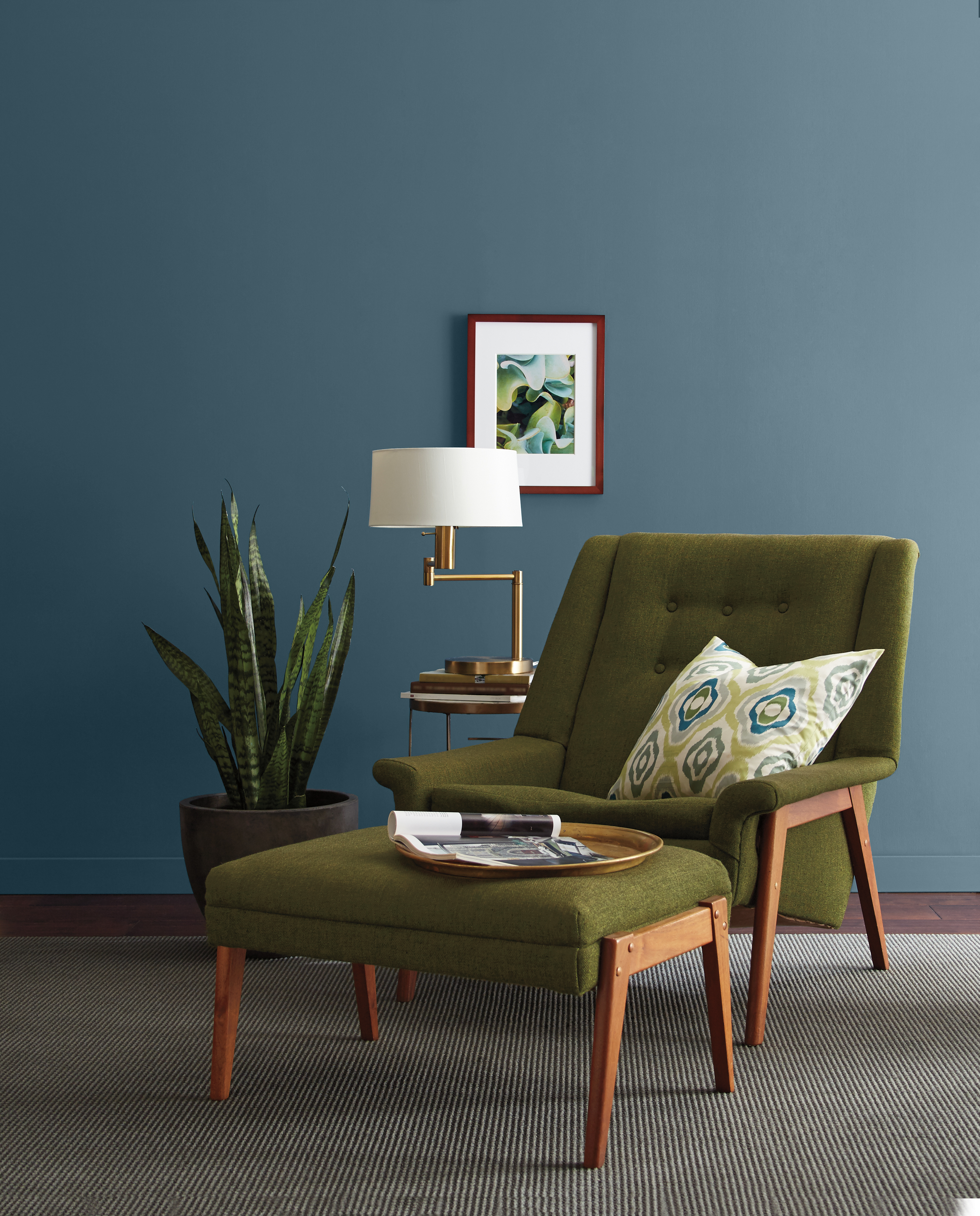 Wall painted in a dark blue colour, styled with a retro olive-green chair and décor pieces