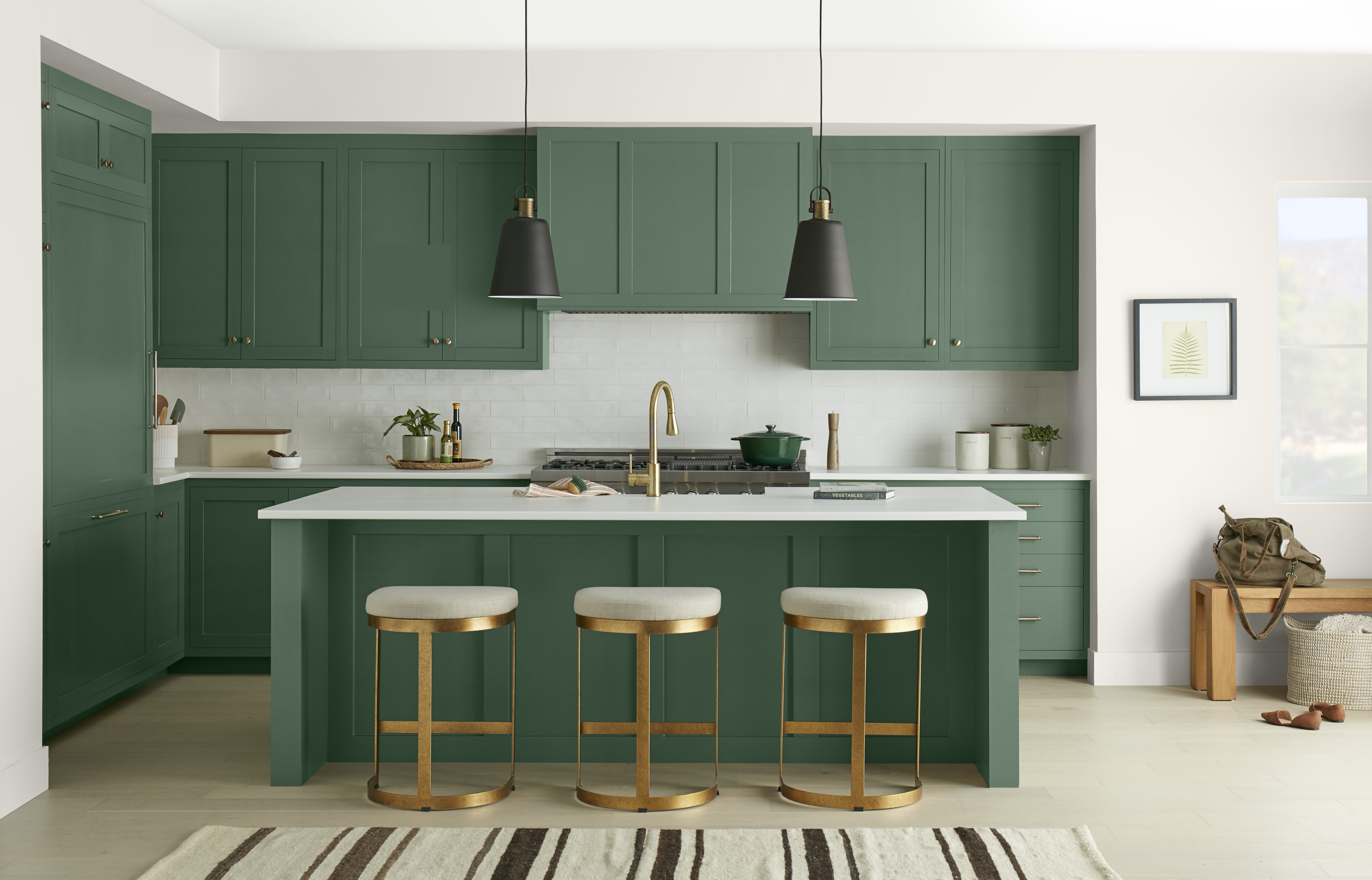 A kitchen with cabinets and an island painted in a deep green colour, styled with modern black and gold finishings.