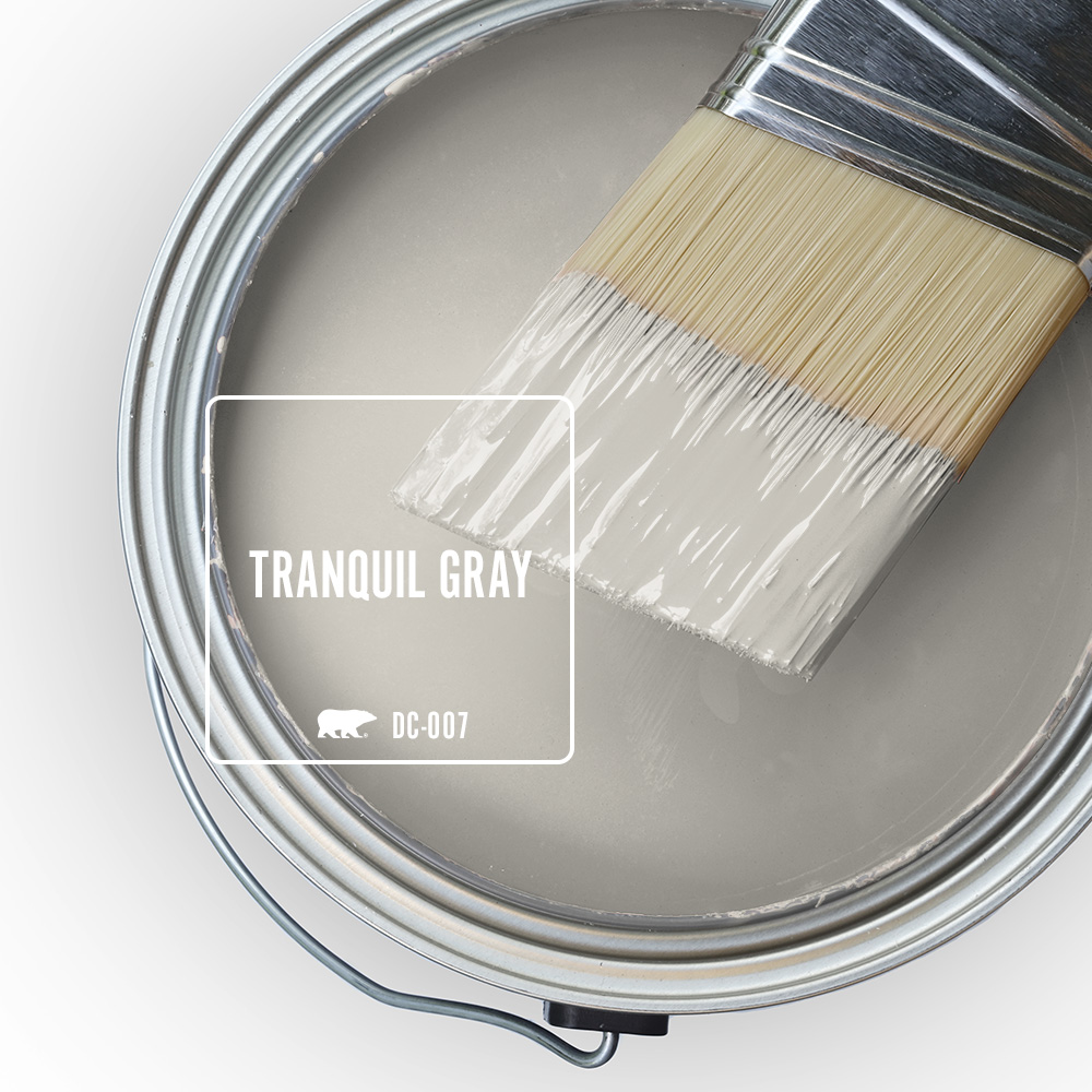 An open paint can with a paintbrush sitting on top. The colour in the can is Tranquil Gray.