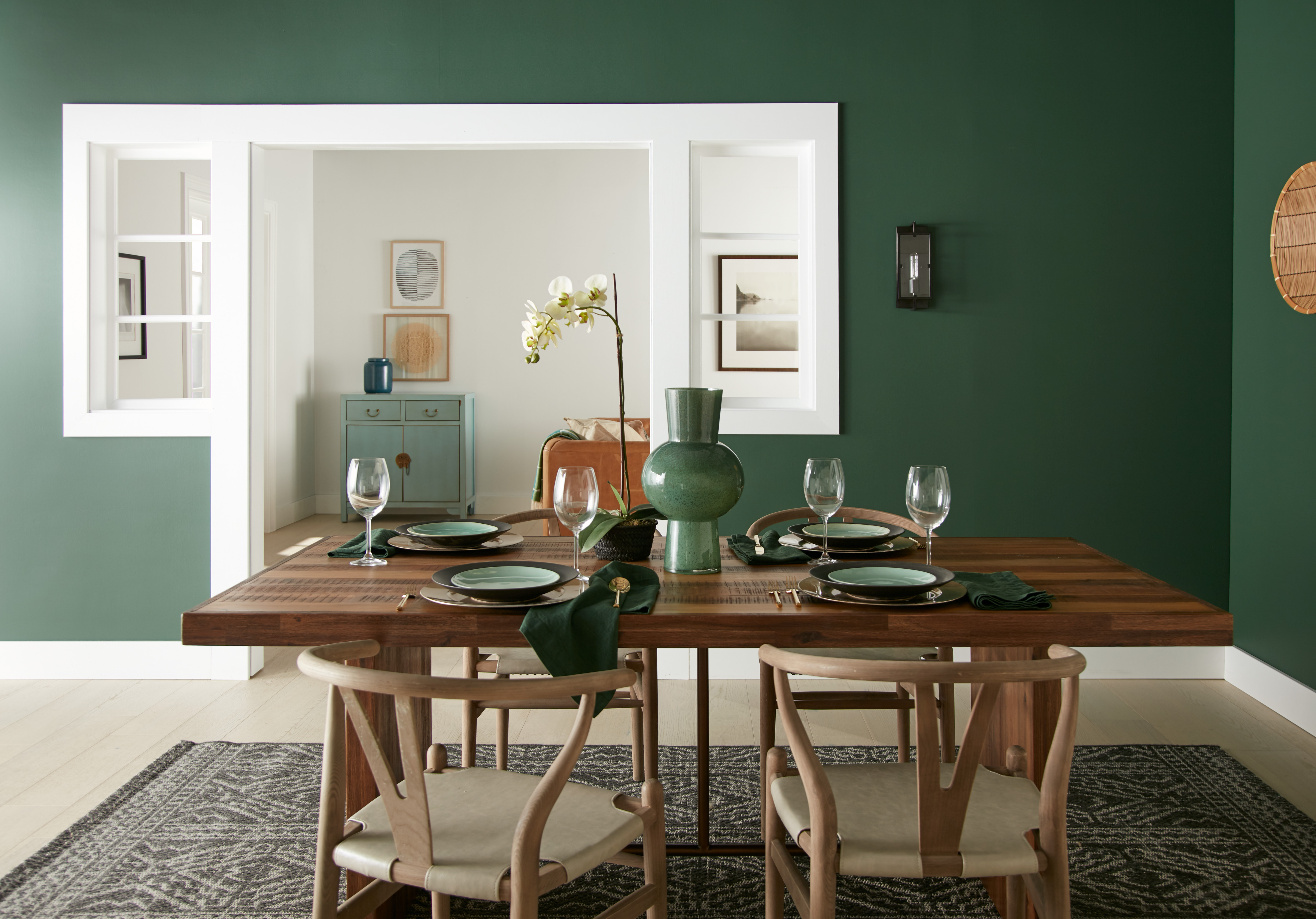 A dining room with walls painted in a deep green colour and a mix of light and dark wood dining table and chairs in the middle.