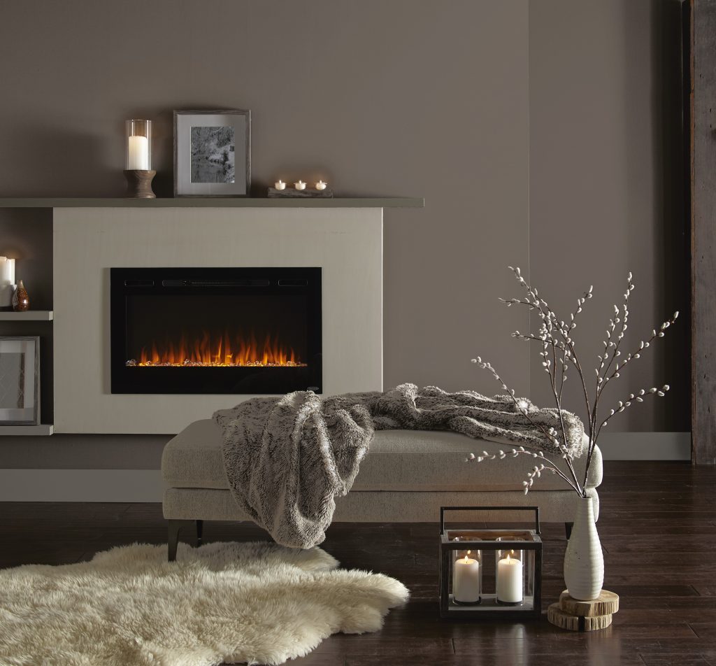 A closeup of a cozy living room with walls painted in Kindling, styled with candles and picture frames on the fireplace mantle