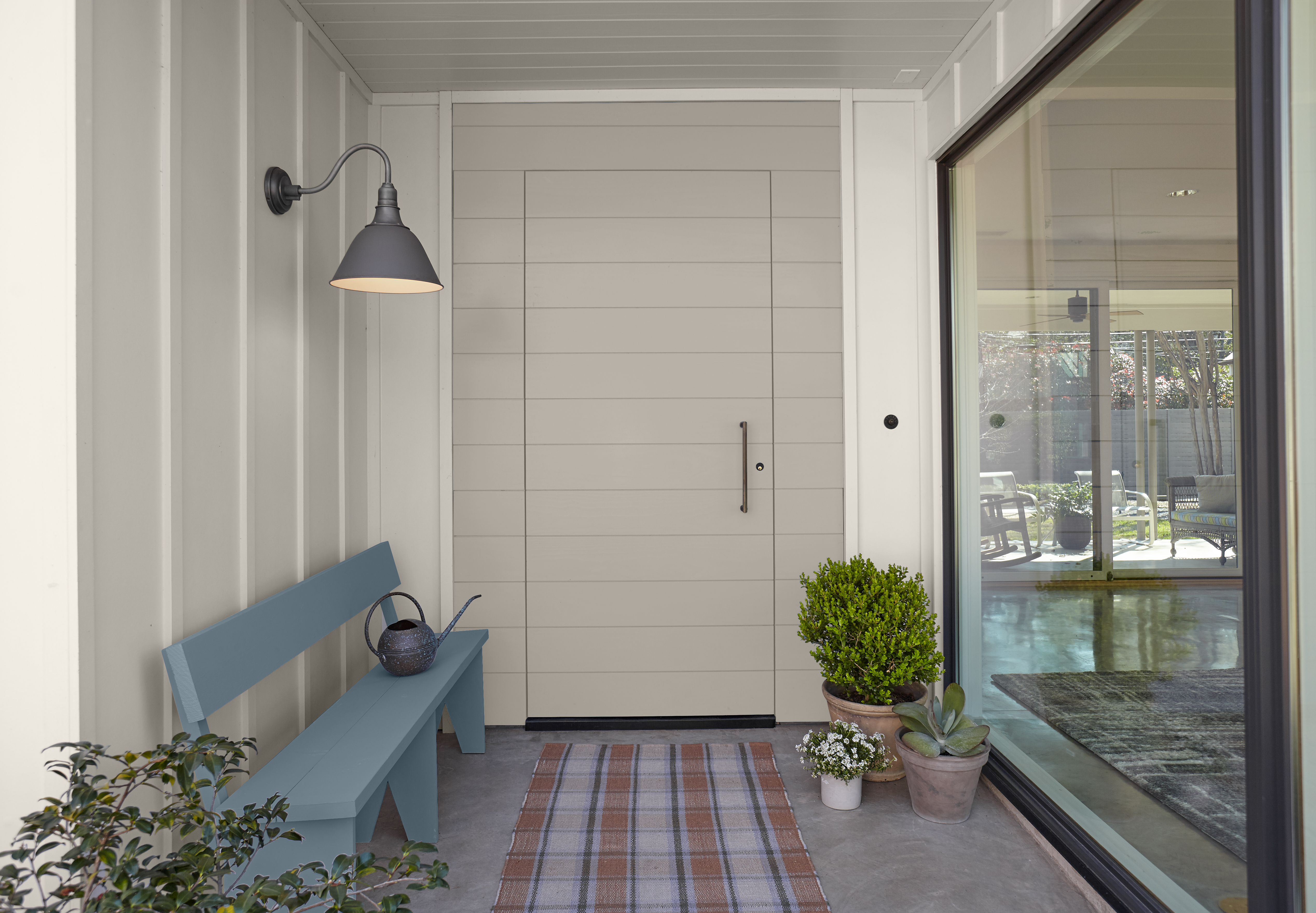 An outdoor entryway with walls painted in a light greige colour and a modern door in a darker greige colour, styled with a bench painted in blue