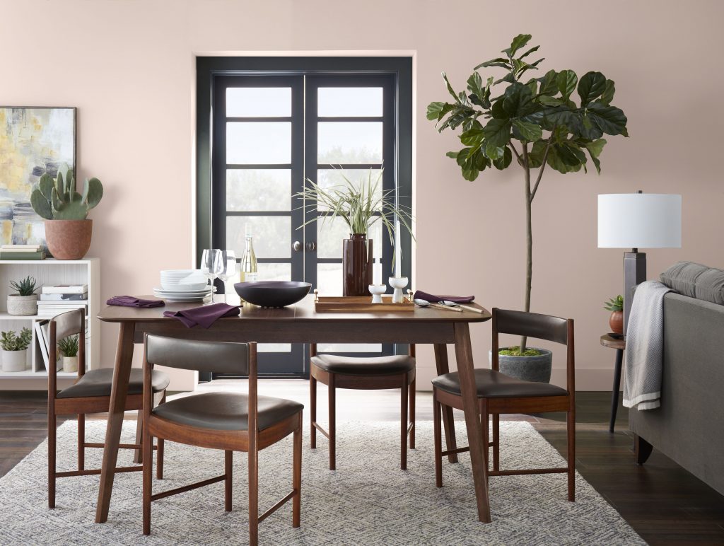A dining room with walls painted in a soft pink colour and styled with mid-modern century furniture