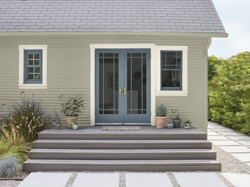 The exterior of a house with siding painted in Jungle Camouflage and a pop of colour on the window and door frames in Adirondack Blue