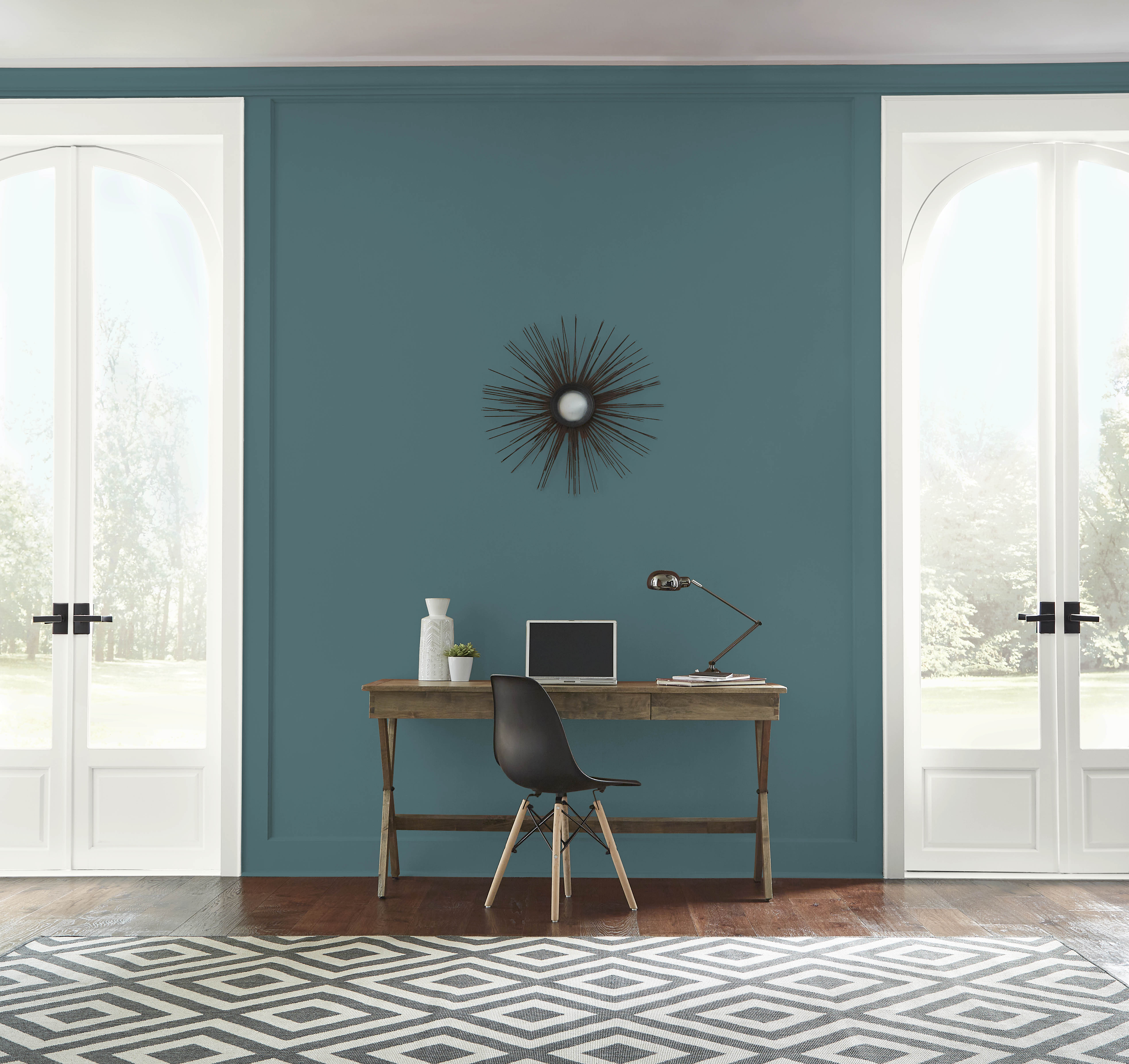 A bright living room with walls in the colour Sophisticated Teal, styled with a wood desk and chair positioned in between two sets of white French doors
