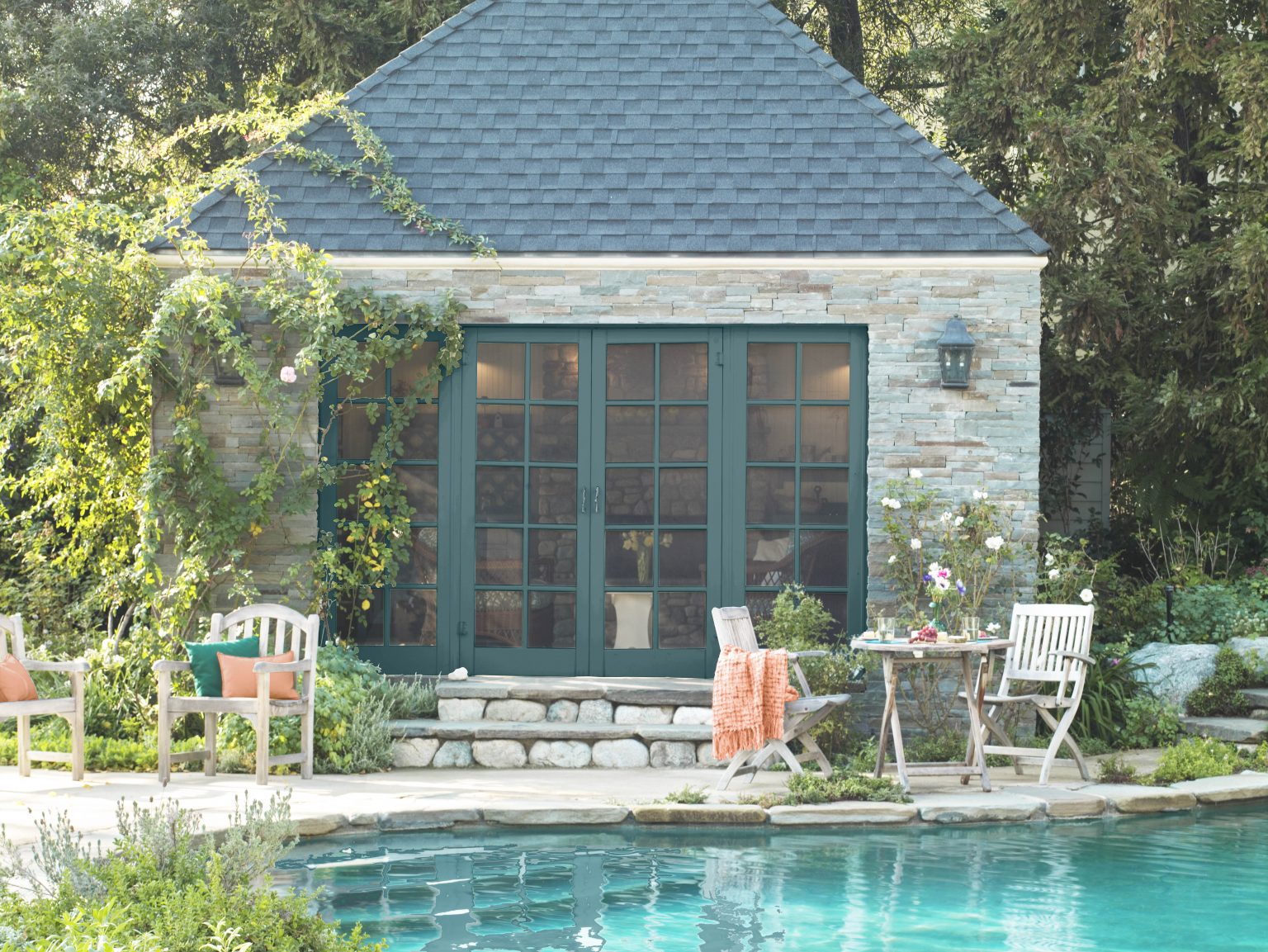 A brick exterior house with trim in the colour Sophisticated Teal, along with a patio set and pool in the foreground