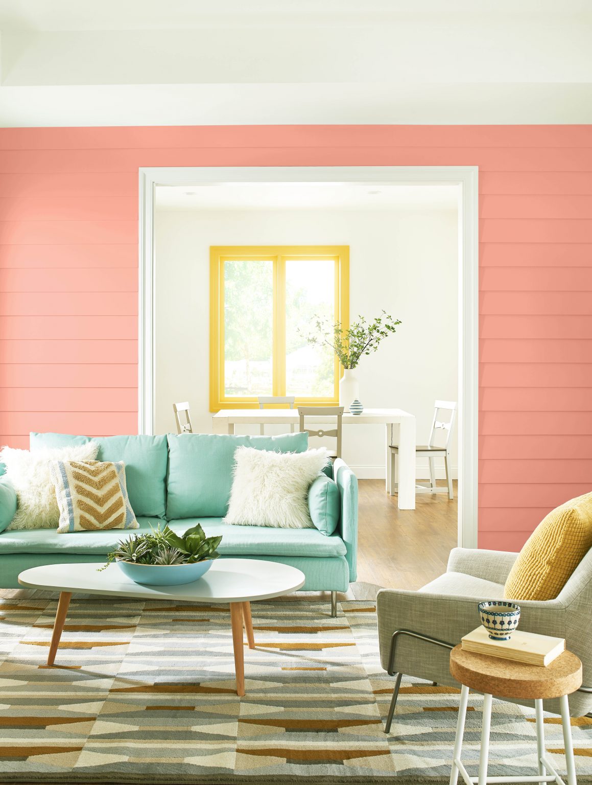 A coastal living room with walls in the colour Peach Mimosa, window trim in Radiant Sun, and styled with aqua and neutral accents 