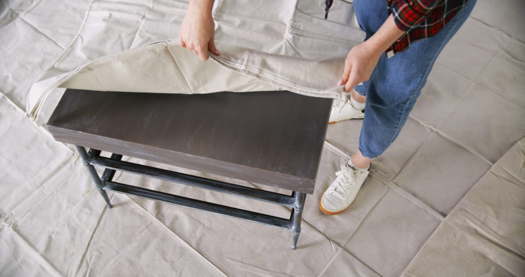 A person covering the top of a table with a drop cloth