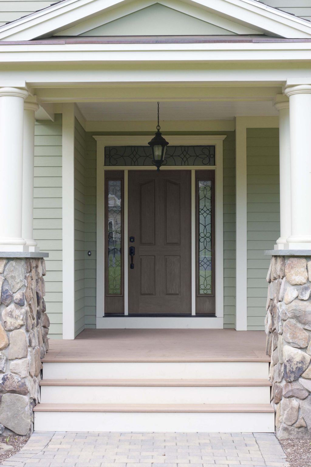 The exterior of a house with muted green siding and white trim, and the front door stained in the colour Cordovan Brown