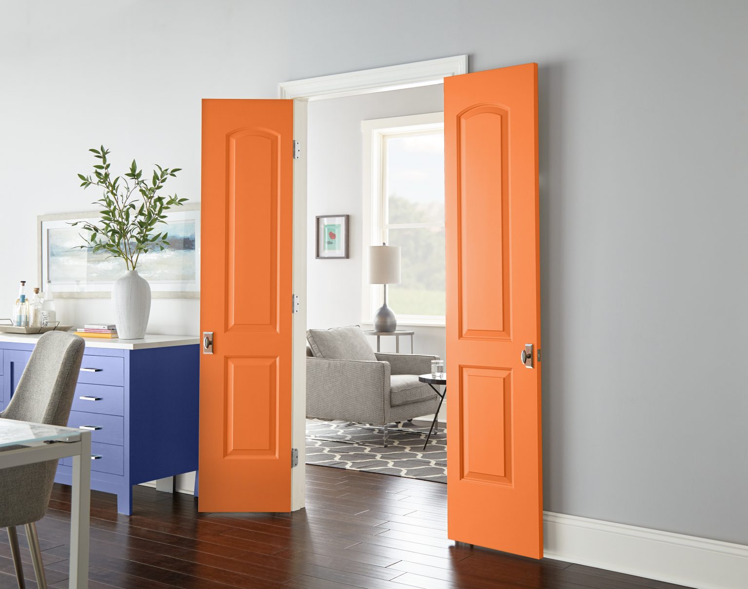 A dining room with a console in the colour Lavender Sky and doors in the colour Tart Orange opening into a living room area