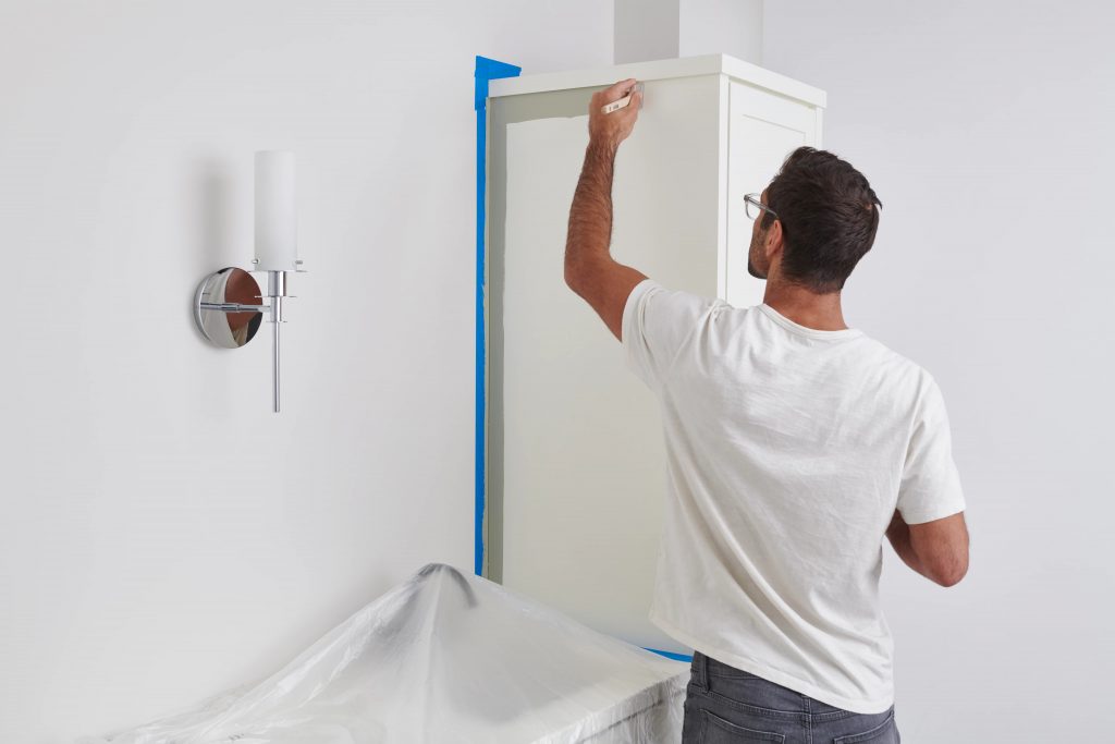 A man using a brush to apply paint to the edges of the bathroom cabinets