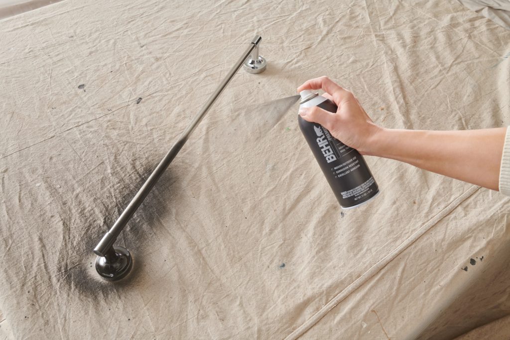 A closeup of a hand holding a spray paint can, applying spray paint to a towel rack