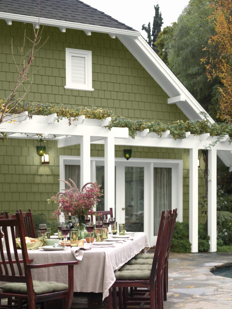 A view into a back patio with a dinner party setup, set against a house exterior painted in the colour Secret Meadow