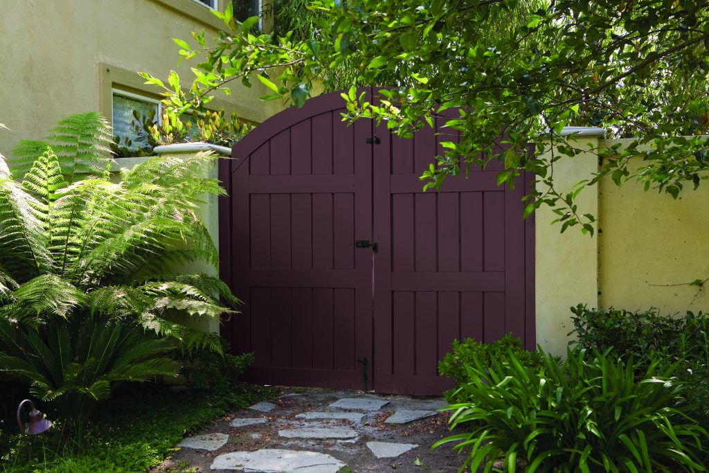 A wooden gate painted in the colour Divine Wine, partially covered by outdoor greenery
