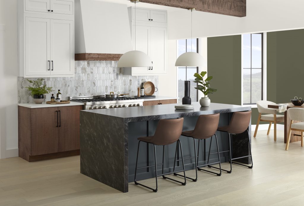 An open concept home layout with a kitchen and dining room area; the kitchen island is black and the dining room has an accent wall in a dark olive green colour