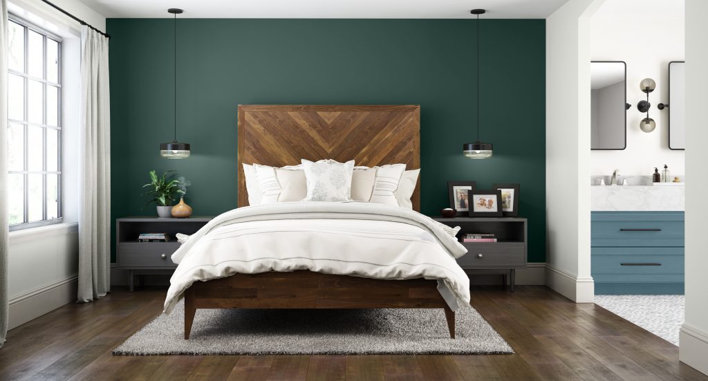 A modern bedroom and bathroom with a dark green accent wall and blue cabinets 