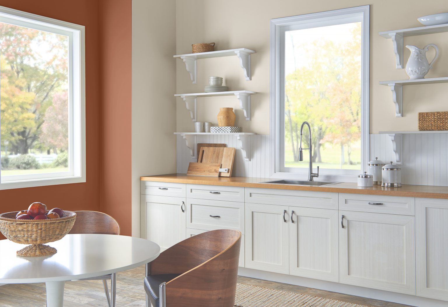 A kitchen with neutral walls and cabinets with an accent wall on the left in the colour Orange Flambe