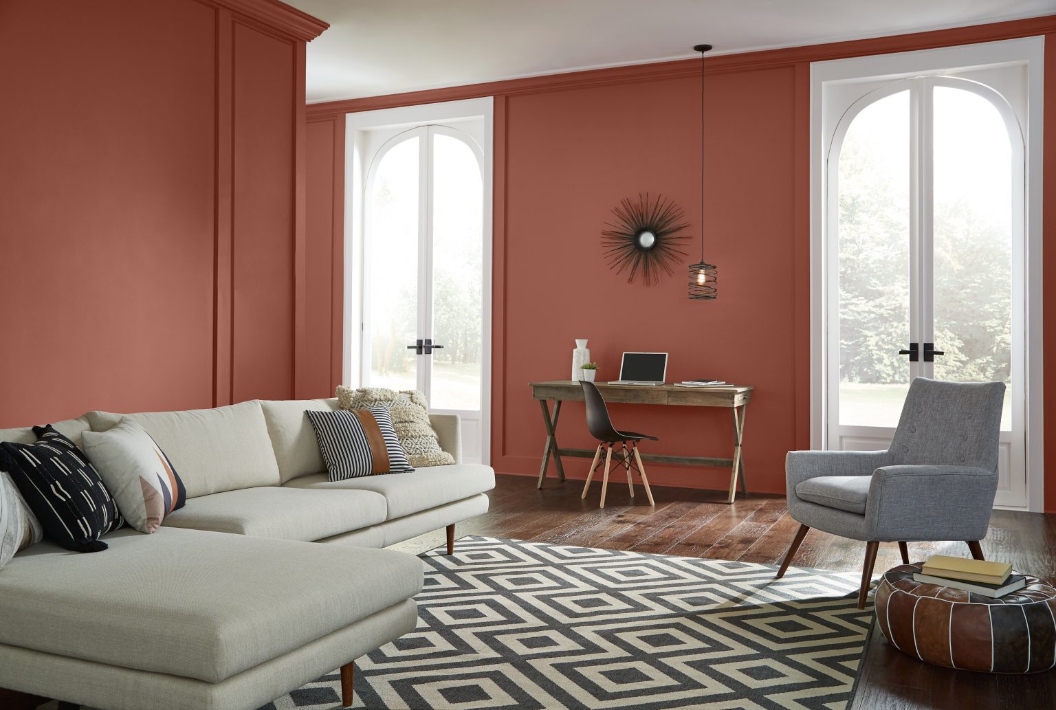 A living room with walls painted in a warm red, styled with a geometric rug and neutral furniture 
