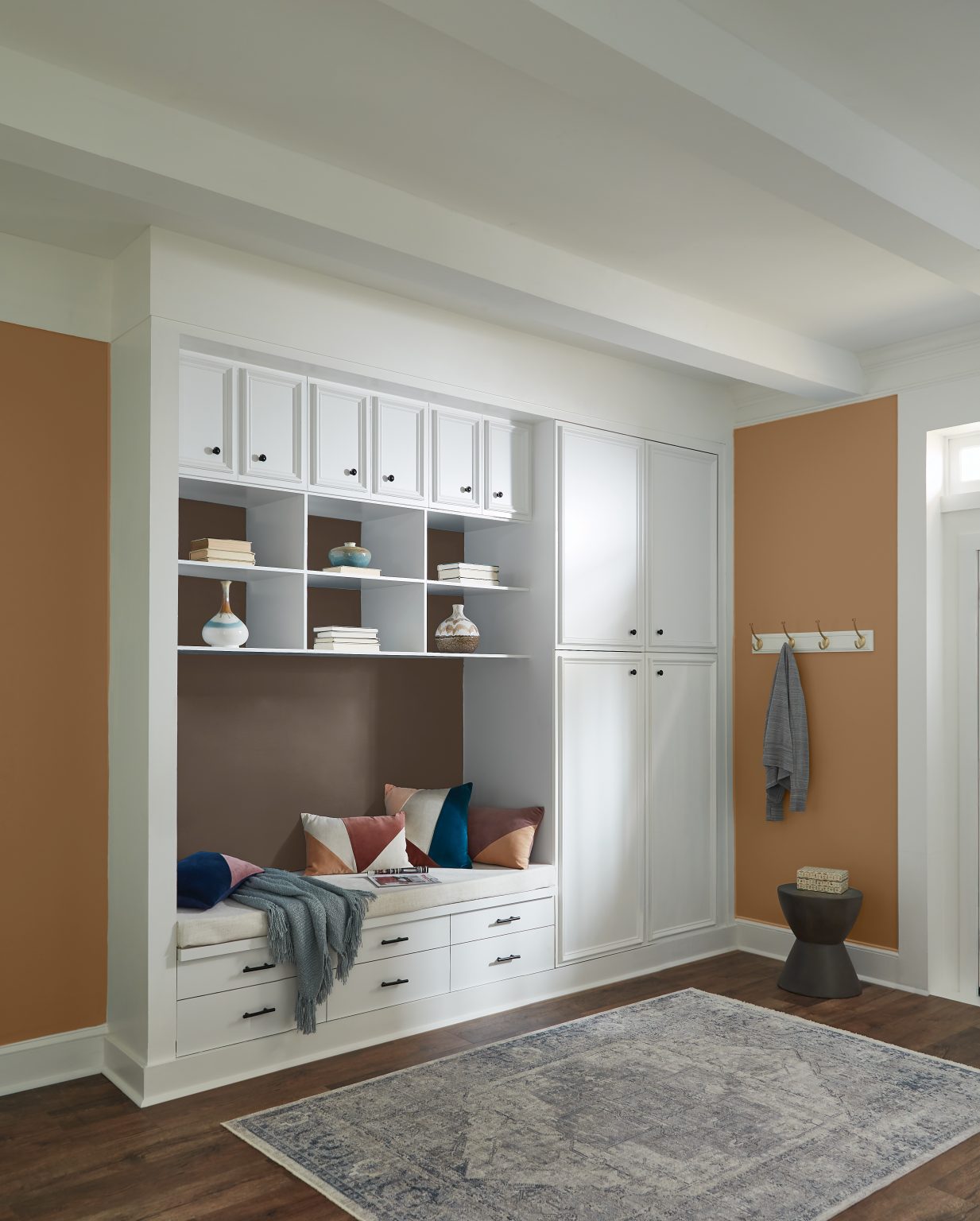 An entryway with walls painted in a gold-brown, with a white built-in closet and seating bench