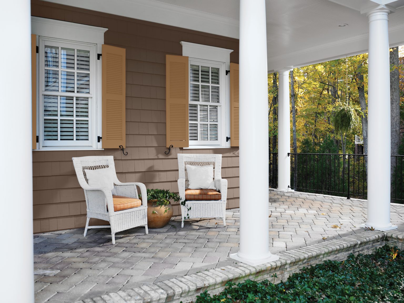 The exterior of a home, with siding in a rich brown and styled with white patio furniture 